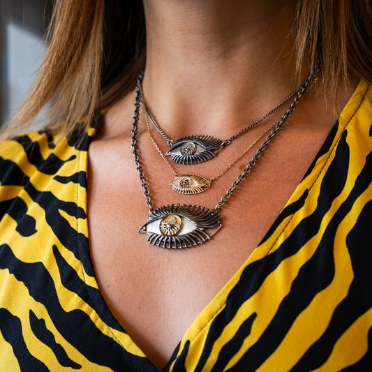 Close-up of a person wearing multiple eye-shaped necklaces with a yellow and black patterned top.