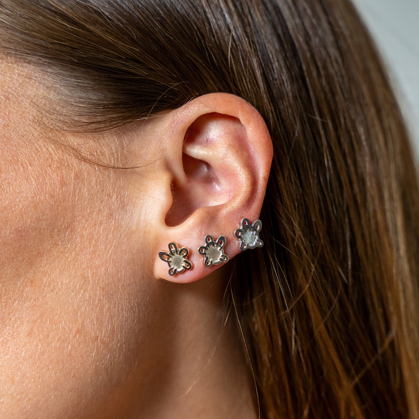 Close-up of an ear wearing three silver flower-shaped earrings.