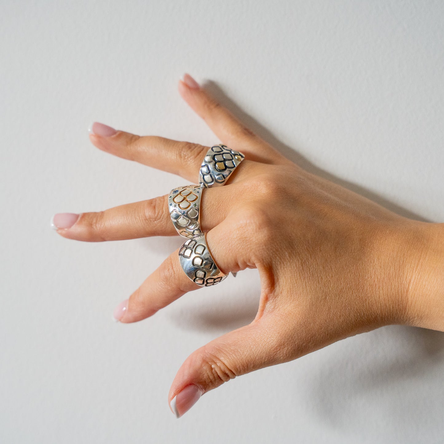 Hand wearing three silver rings with diamonds and gold on a light white background