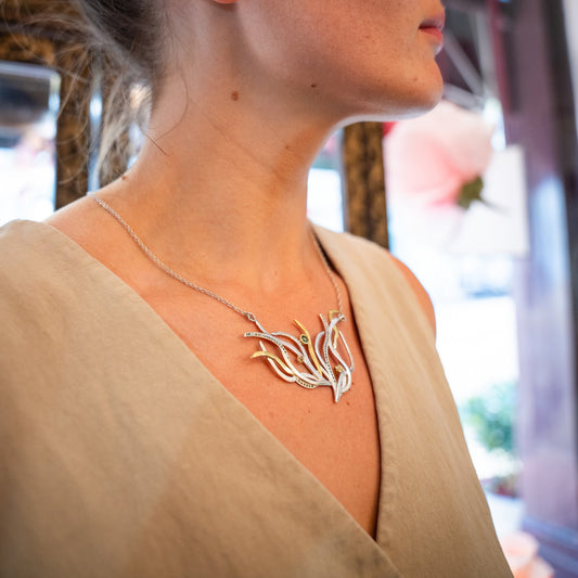 Necklace with a leaf-like pendant worn by a person in a beige top.