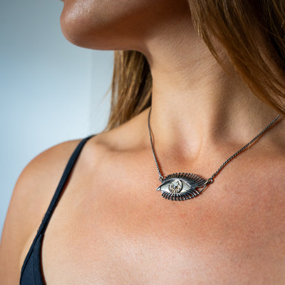 Close-up of a necklace with an eye pendant on a person's neck against a light background