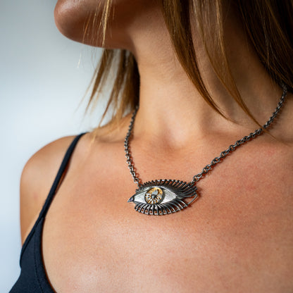 Close-up of a person wearing a unique necklace with an eye design.