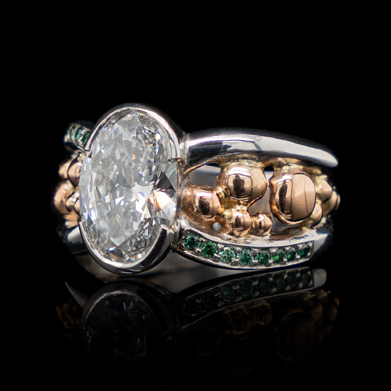 Gold and silver ring with a large diamond and smaller emerald stones on a black background