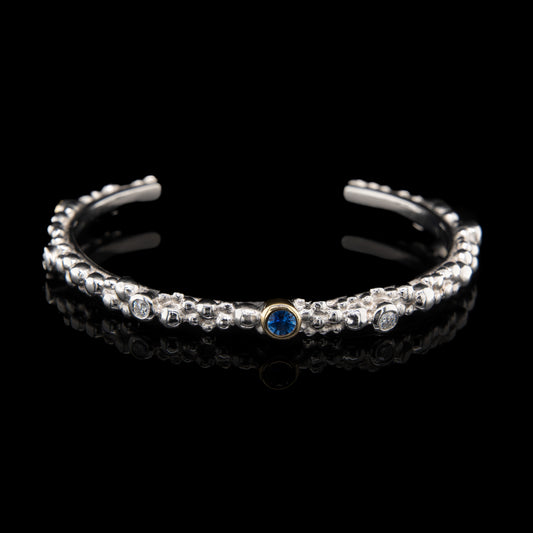platinum cuff bangle with blue sapphires and diamonds on a black background.