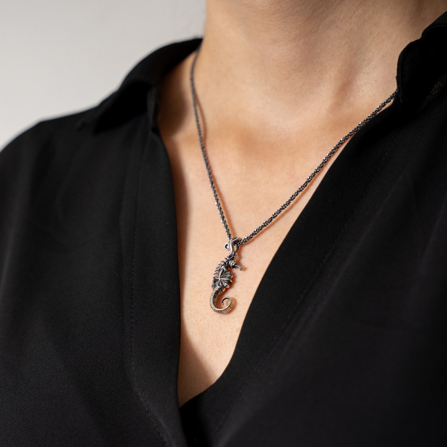 Necklace with a seahorse pendant worn by a person in a black top.