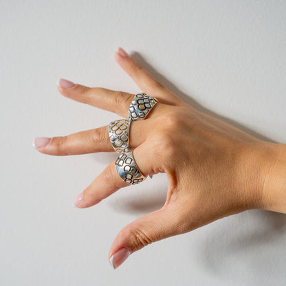 Hand wearing three silver rings with diamonds and gold on a light white background
