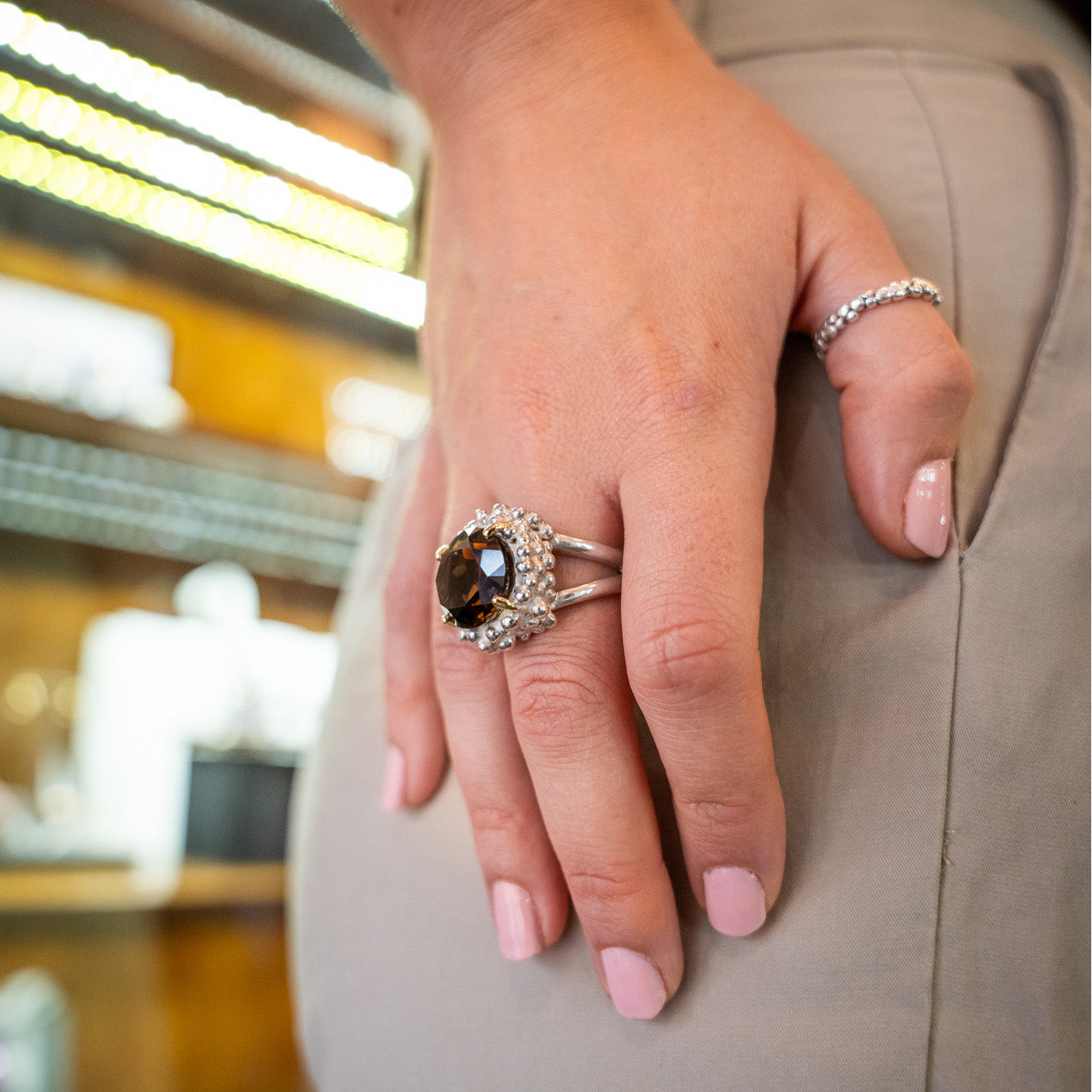 Close-up of a hand wearing a ring with a brown gemstone on a blurred indoor background