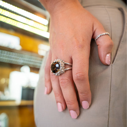 Close-up of a hand wearing a ring with a brown gemstone on a blurred indoor background